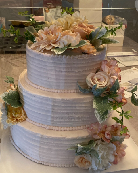 Three-tiered wedding cake with floral decorations on a clear stand.