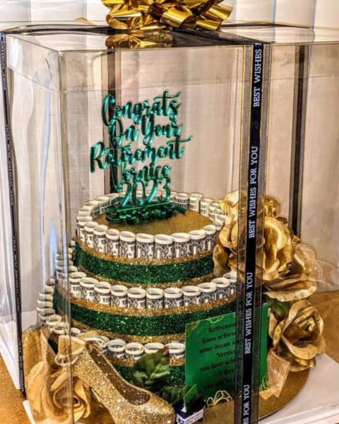 Decorative cake with green and gold colors in a clear display case.