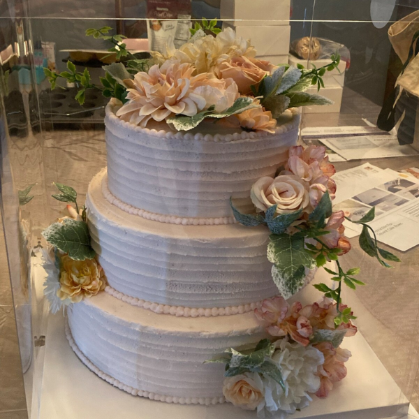 Three-tiered wedding cake with floral decorations on a clear stand.