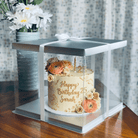 Birthday cake with floral decorations in a transparent box on a wooden table.
