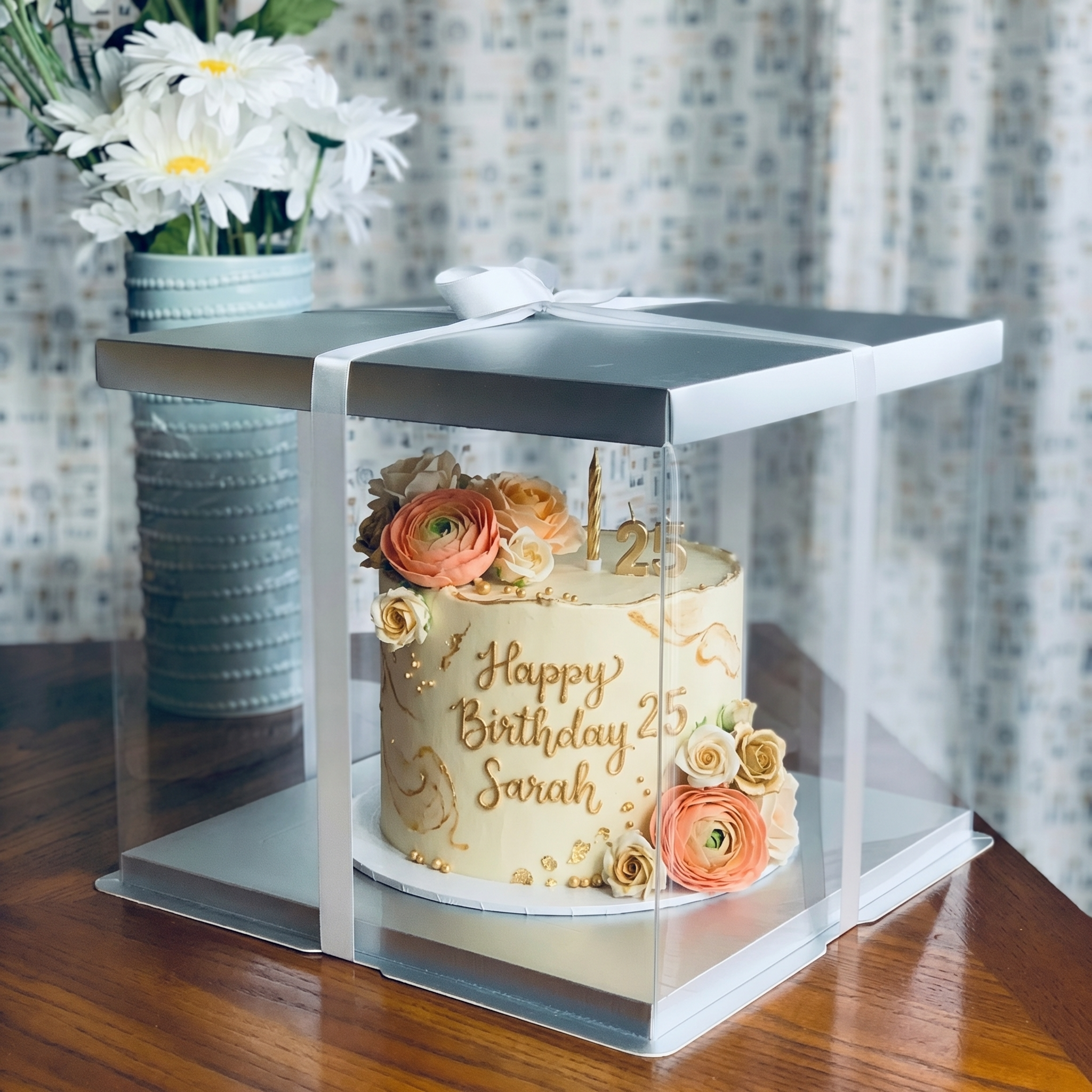Birthday cake with floral decorations in a transparent box on a wooden table.