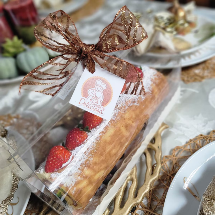 Pastry with strawberries in a clear box with a decorative bow on a table setting.
