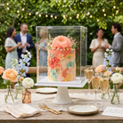 Decorative cake with floral decorations on a wooden table outdoors with people in the background.